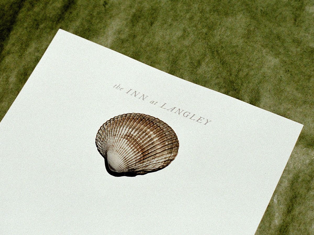 Pale letterhead printed “the Inn at Langley” with a cockle shell resting on it, laid on green fabric.