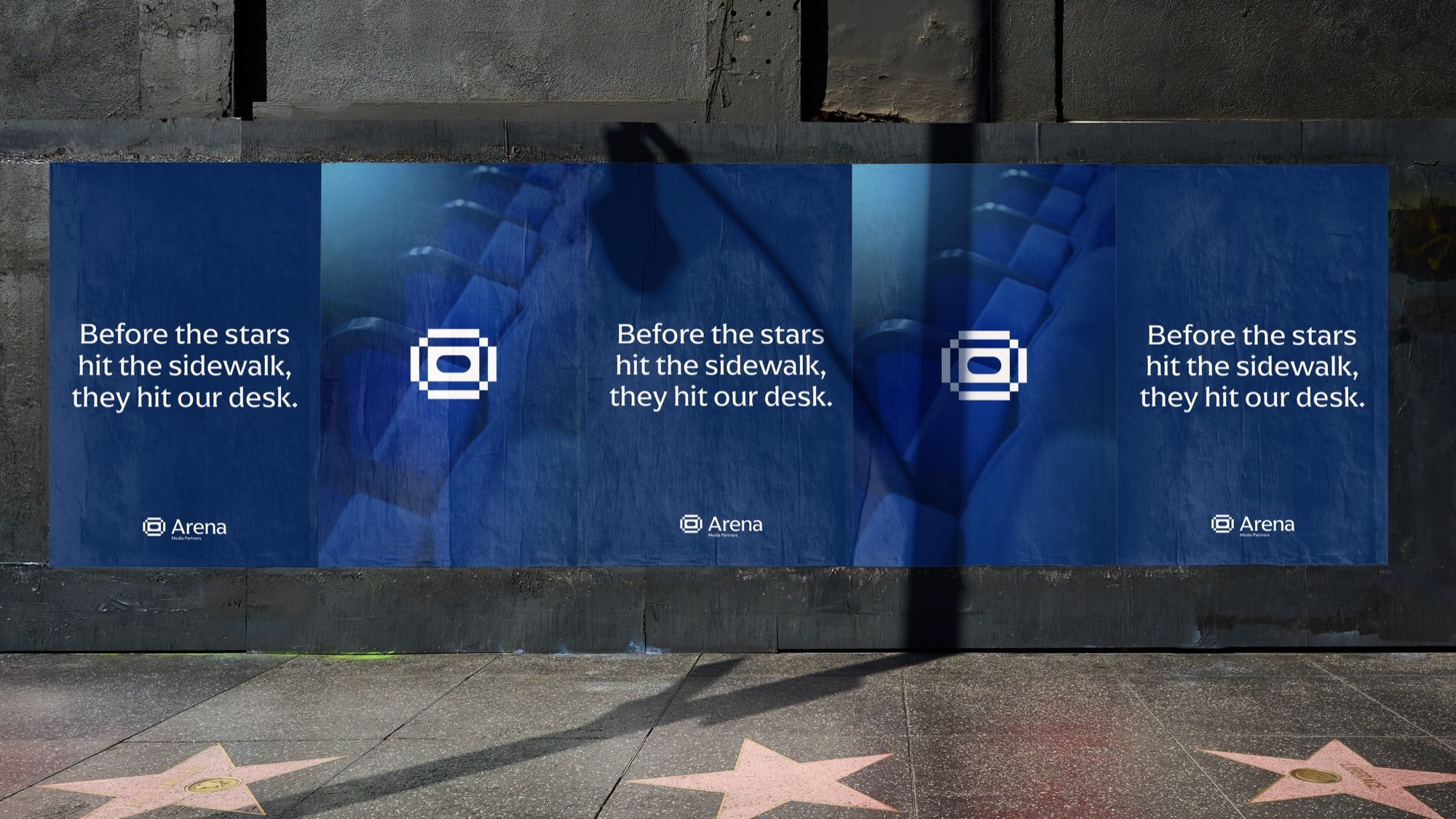 Arena posters pasted along a wall above a pavement of stars, reading “Before the stars hit the sidewalk, they hit our desk.”
