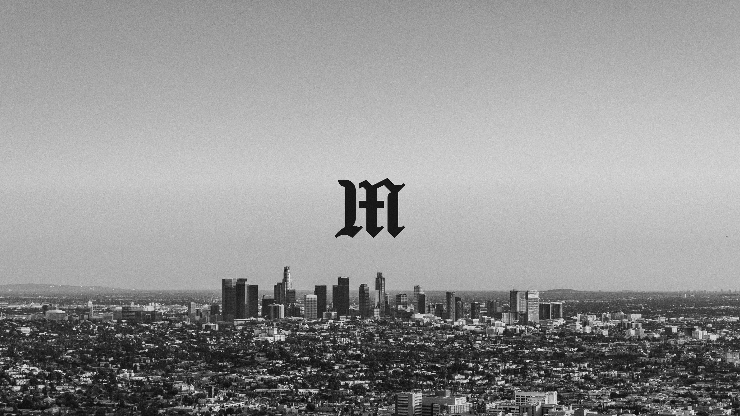 The blackletter M mark floating over a black-and-white view of the Los Angeles skyline.